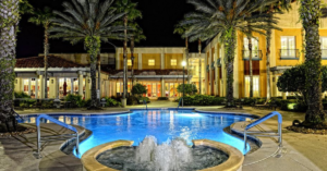 water fountain and pool lit up at night surrounded by palm trees